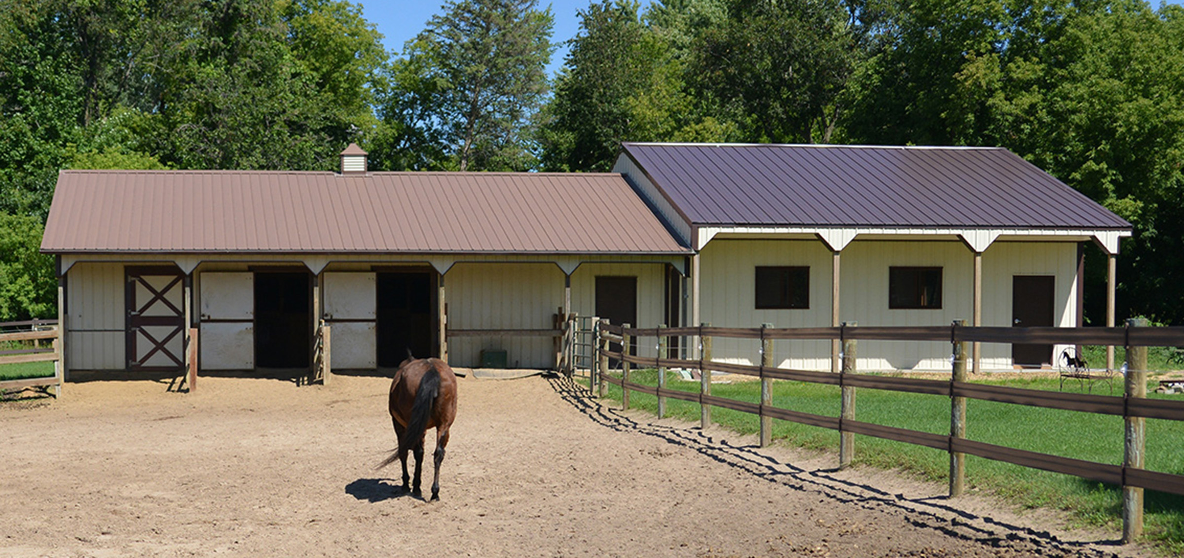Cream and brown post frame equine building with a horse walking into it
