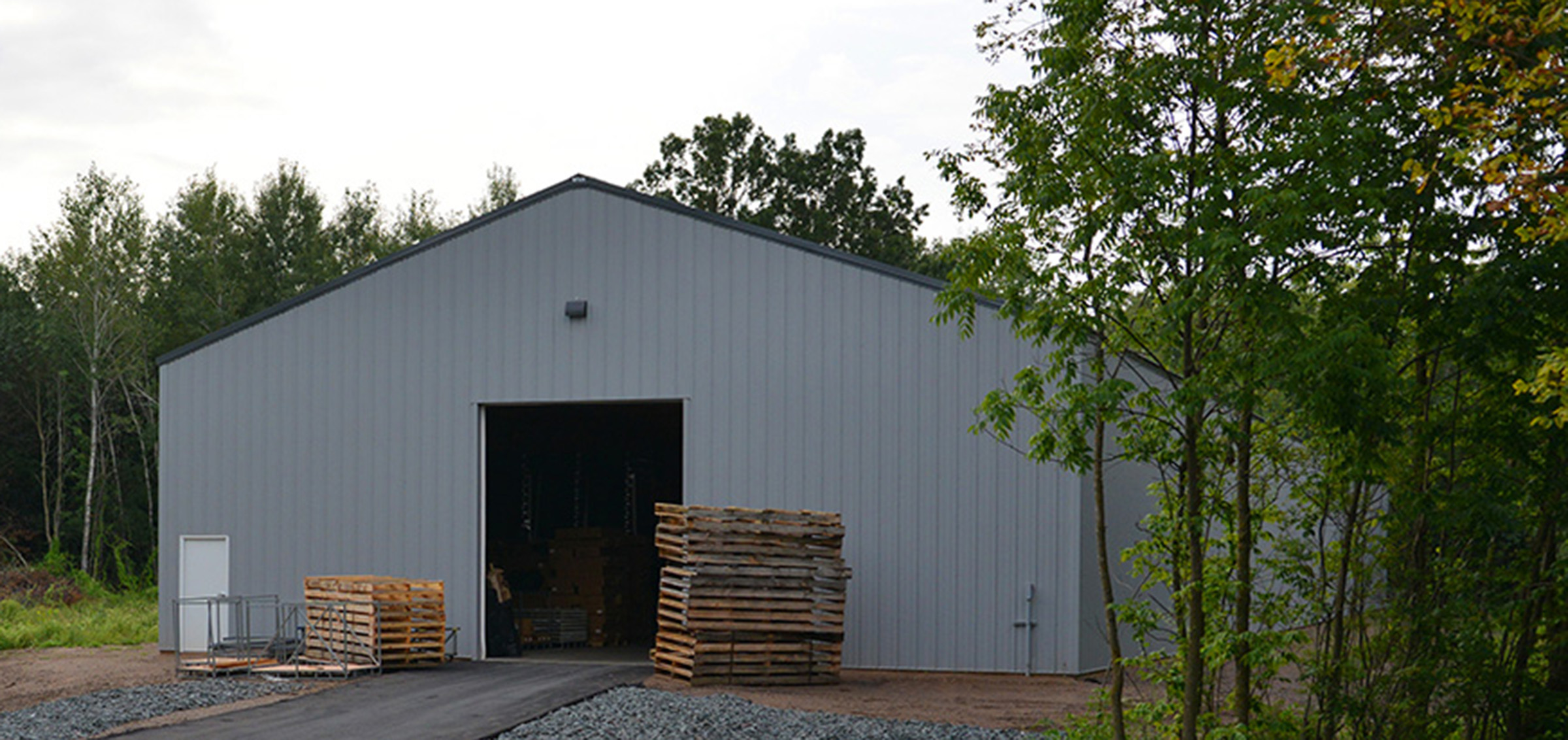 gray post frame commercial storage building with two stacks of wood palettes framing a garage door
