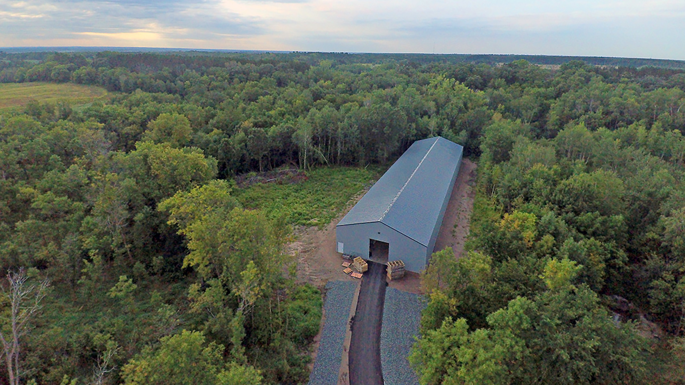drone view of a gray post frame storage building in the forest